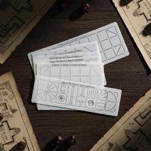 May include: A collection of white stencils for tabletop role-playing games, showing detailed room layouts and designs. The stencils are on a dark wooden surface, with dice and map fragments around.