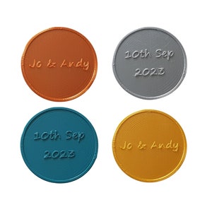 May include: Four round, metallic tokens with engraved text. Two tokens are copper-coloured and read "Jo & Andy". Two tokens are silver-coloured and read "10th Sep 2023".