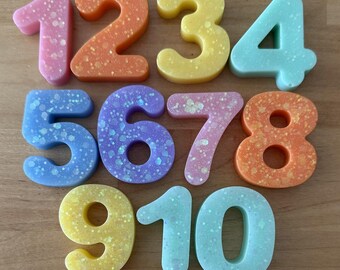 May include: Colorful number and donut-shaped beads. The numbers 1 through 10 are in various colors, including pink, orange, yellow, and blue, with a speckled design. Below are donut-shaped beads in matching colors.