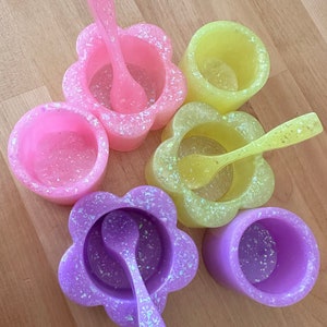 May include: Five small flower-shaped bowls with matching spoons. The bowls are in shades of pink, yellow, and purple with iridescent glitter.