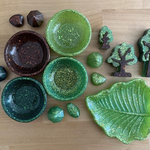 May include: An assortment of decorative items in shades of green and brown, including small bowls, geometric shapes, leaf-shaped trays, and tree-shaped ornaments. The items have a speckled design, creating a natural, earthy aesthetic.