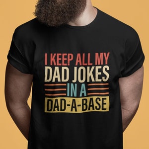 Könnte beinhalten: Ein schwarzes T-Shirt mit einer Grafik im Retro-Stil, auf dem "Ich bewahre all meine Papa-Witze in einer Papa-Datenbank auf" steht.