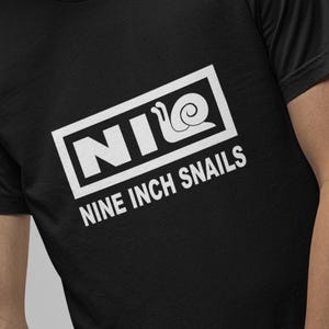 May include: Black t-shirt with a white graphic that reads "NIO" inside a rectangle, with a snail graphic, and the words "NINE INCH SNAILS" below. The shirt is a crew neck style.