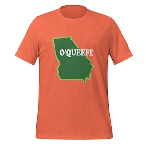 May include: Orange t-shirt featuring a green outline of the state of Georgia with the word "O'QUEEFE" in white block letters. The t-shirt is made of a soft material and has short sleeves and a crew neck.