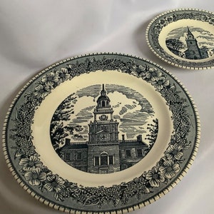 Può includere: Un set di due piatti in ceramica blu e bianca con un'illustrazione in bianco e nero di un edificio con una torre dell'orologio. I piatti hanno un bordo floreale.