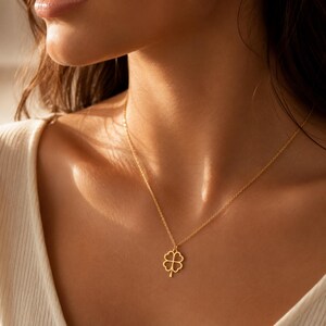 May include: A gold-toned necklace featuring a delicate chain and a small, four-leaf clover pendant. The pendant has a cut-out design with thin, smooth edges, suspended centrally from the fine metal chain resting against the collarbone area.