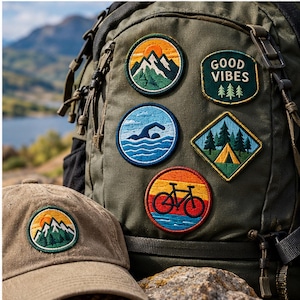May include: An olive green backpack and a tan baseball cap decorated with embroidered patches. The patches feature a mountain landscape, the text GOOD VIBES with pine trees, a person swimming in blue water, a tent in a forest, and a bicycle.
