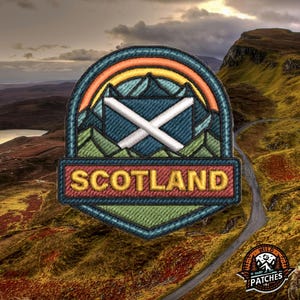 Könnte beinhalten: Gestickter Aufnäher mit dem Wort "SCOTLAND" in Rot. Der Aufnäher zeigt die schottische Flagge, einen Regenbogen und eine Berglandschaft. Der Hintergrund zeigt eine Landschaft mit einer kurvenreichen Straße und einem Logo "WILD PATCHES".