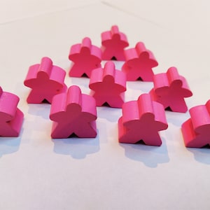 Può includere: Un gruppo di dieci pedine da gioco meeple rosa, disposte a forma di triangolo su una superficie bianca.