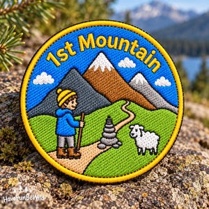 Può includere: Una toppa ricamata circolare che raffigura un cielo blu con nuvole bianche, montagne marroni e grigie e la scritta 1st Mountain. Un escursionista con berretto giallo e giacca blu tiene un bastone su un sentiero vicino a un ometto di pietra e una pecora bianca.