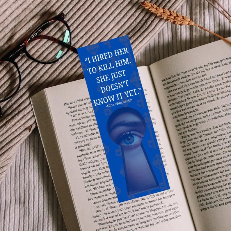 Pode incluir: Marcador de livro azul com o texto "I Hired Her to Kill Him. She Just Doesn't Know It Yet." e um design de olho, colocado em um livro aberto com &oacute;culos.