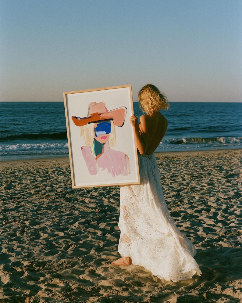 Puede incluir: Una impresi&oacute;n art&iacute;stica rectangular enmarcada que presenta una pintura abstracta de una figura con un sombrero de ala ancha. La obra utiliza pinceladas audaces en tonos rosa, marr&oacute;n y un bloque azul sobre los ojos, sobre fondo blanco.