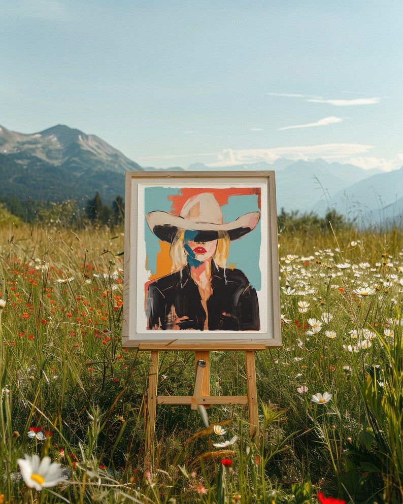 May include: A framed painting of a woman wearing a wide-brimmed hat and a black jacket. The painting is set against a blue and orange background and is displayed on an easel in a field of wildflowers.