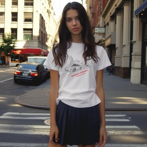 May include: A white t-shirt with a black and white illustration of a car and the text "Amalfi Coast Vintage Show". The person wearing the shirt is standing on a city street.