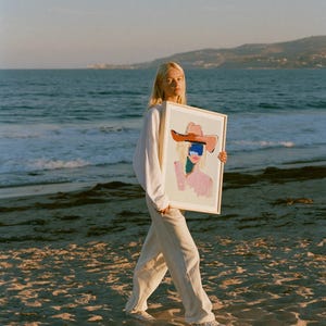 Puede incluir: Una l&aacute;mina de arte rectangular enmarcada que presenta una ilustraci&oacute;n abstracta de una figura con un sombrero de ala ancha. La obra utiliza una paleta de tonos rosa suave, azul profundo y marr&oacute;n c&aacute;lido sobre un fondo crema, en un marco de madera clara.