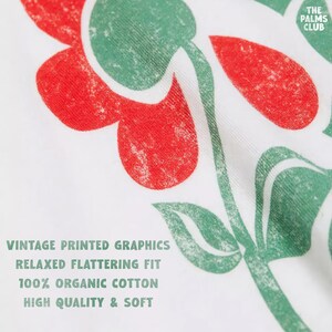 May include: White t-shirt with a green and red floral print. The text "THE PALMS CLUB" is printed in the top right corner. The text "VINTAGE PRINTED GRAPHICS", "RELAXED FLATTERING FIT", "100% ORGANIC COTTON", and "HIGH QUALITY & SOFT" is printed in green at the bottom of the shirt.