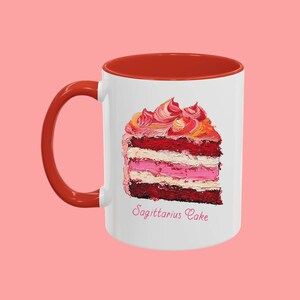 May include: White ceramic mug with a red rim and handle. The mug features a colorful illustration of a slice of cake with the text "Sagittarius Cake" printed below.