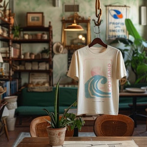 K&ouml;nnte beinhalten: Ein cremefarbenes Kurzarm-T-Shirt mit einem Grafikdruck einer blauen Meereswelle, einer rosa Sonne und dem vertikalen Text "POSITANO" und "SURF", wobei "ITALY CAMP 1980" unter dem Wellenmotiv auf der Vorderseite des Kleidungsst&uuml;cks gedruckt ist.