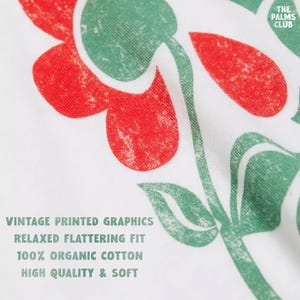 K&ouml;nnte beinhalten: Ein wei&szlig;er Stoff mit einem verwaschenen roten und gr&uuml;nen Blumen-Grafikdruck. Der Text lautet: VINTAGE PRINTED GRAPHICS, RELAXED FLATTERING FIT, 100% ORGANIC COTTON, HIGH QUALITY & SOFT, sowie THE PALMS CLUB in der oberen rechten Ecke.