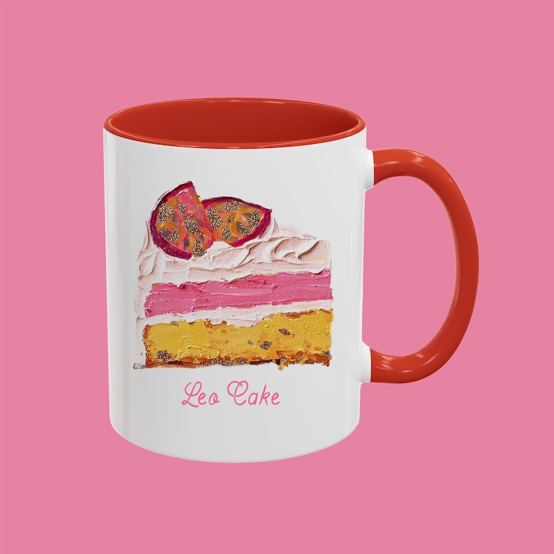 May include: White ceramic mug with a red rim and handle. The mug features a painting of a slice of cake with pink frosting and passion fruit on top. The text "Leo Cake" is printed below the cake.