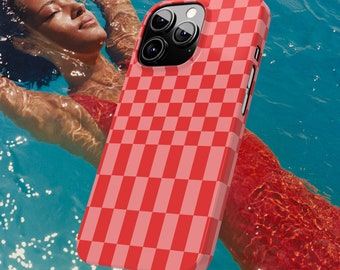 Puede incluir: Una funda de teléfono a cuadros rojos y rosas. La funda se muestra frente a una persona nadando en una piscina. La funda tiene un acabado brillante y un borde elevado alrededor de la cámara.
