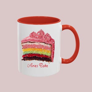 May include: White ceramic mug with a red rim and handle. The mug features a colorful cake with pink frosting and the text "Aries Cake".