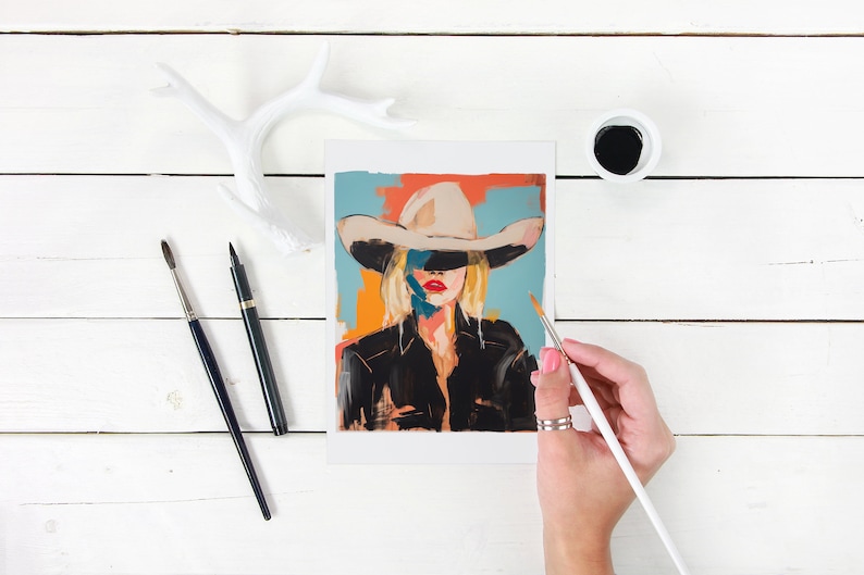 May include: A painting of a woman wearing a white cowboy hat with a blue, orange, and red background. The woman is wearing a black jacket and has blonde hair. The painting is being worked on with a paintbrush.
