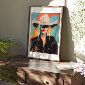 May include: A framed painting of a woman wearing a white cowboy hat. The woman's face is partially obscured by the hat, and her eyes are closed. The background of the painting is a colorful abstract design.
