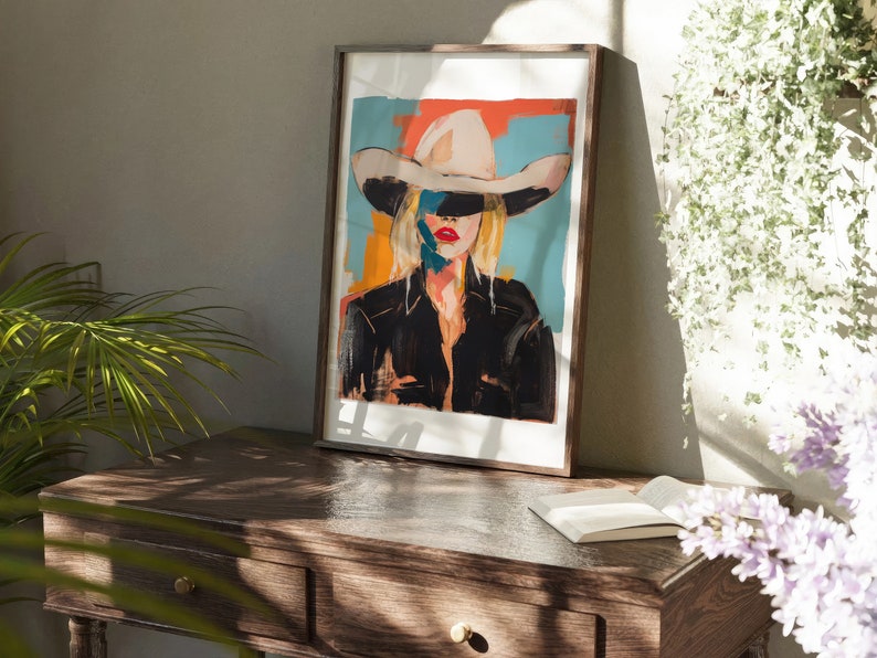 May include: A framed painting of a woman wearing a white cowboy hat. The woman's face is partially obscured by the hat, and her eyes are closed. The background of the painting is a colorful abstract design.