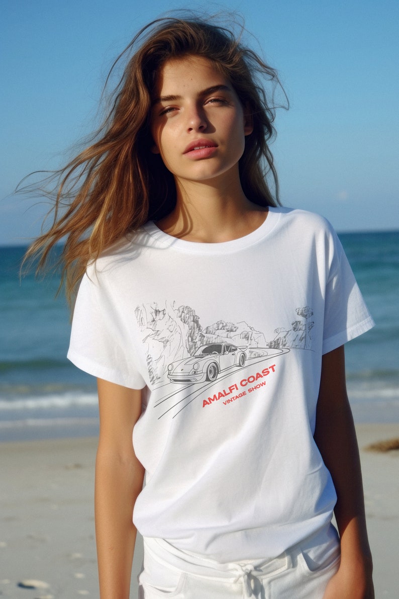 May include: White t-shirt with a black and white illustration of a car driving on a winding road with the text "Amalfi Coast Vintage Show" in red and black.