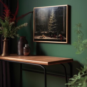 May include: A framed painting of a Christmas tree with ornaments and candles in a dark room. The painting is hanging on a green wall above a wooden table with a black metal frame.