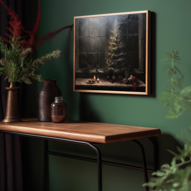 May include: A framed painting of a Christmas tree with ornaments and candles in a dark room. The painting is hanging on a green wall above a wooden table with a black metal frame.