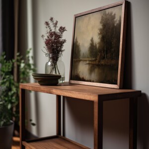 Puede incluir: Una estanter&iacute;a de madera con dos estantes, que presenta una pintura de paisaje enmarcada con un lago y &aacute;rboles. Un jarr&oacute;n con flores secas se encuentra en el estante superior.