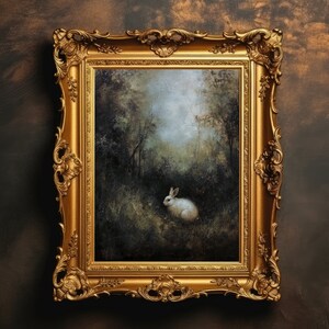 May include: A framed painting of a white rabbit in a forest setting. The rabbit is sitting in the middle of the painting, with trees and foliage surrounding it. The painting is in a gold frame.