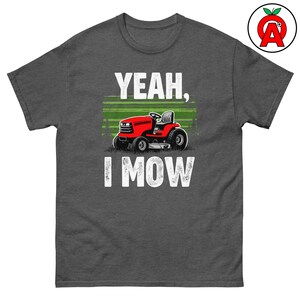Könnte beinhalten: Dunkelgraues T-Shirt mit dem weißen Schriftzug "YEAH, I MOW". Auf dem Shirt ist ein roter Rasentraktor abgebildet, mit grünen und weißen horizontalen Linien darüber. Das T-Shirt ist aus einem schweren Baumwollmischgewebe.