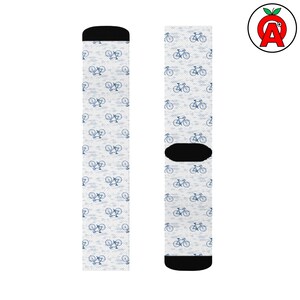 May include: A pair of white socks featuring a repeating pattern of blue bicycles. The socks have black heels and toes, and a black band around the mid-foot. These socks are designed for comfort and style.
