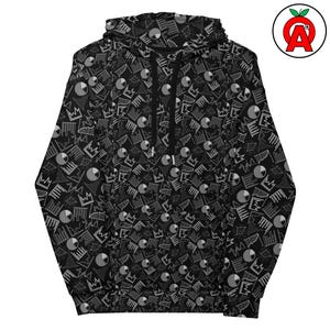 以下が含まれることがあります： 幾何学模様、王冠、円がグレーと白で繰り返される黒いパーカー。パーカーにはドローストリングフードとフロントポケットが付いています。白い「A」が付いた赤いリンゴのロゴが右上隅にあります。