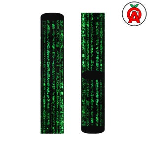 Peut inclure: Paire de chaussettes noires avec un motif de pluie numérique vert, rappelant le film Matrix. Les chaussettes ont un talon et un bout noirs, et un bord côtelé. Le motif est un motif répétitif de caractères verts. Un logo avec une pomme rouge et la lettre "A" est dans le coin supérieur droit.