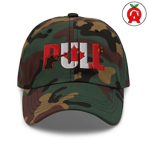 May include: Camouflage baseball cap with the word "PULL" embroidered in red and white. The "U" features a Canadian maple leaf. The "P" shows a person aiming a rifle. A small logo is on the side.