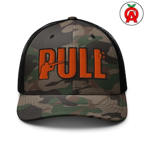 May include: Camouflage trucker hat with the word "PULL" in orange block letters. The "U" features an orange silhouette of a person aiming a shotgun. The hat has a black mesh back and a curved brim.