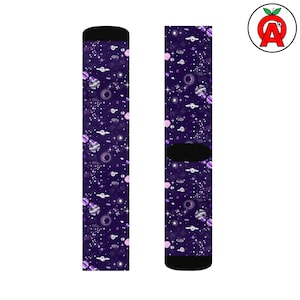 May include: A pair of purple socks with a space-themed pattern. The design includes planets, stars, and UFOs in white and pink. The socks have black heels and toes.