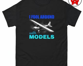 May include: A black short-sleeve t-shirt featuring a white graphic of a small airplane. The text "I FOOL AROUND" is printed in blue above the airplane, and the word "with MODELS" is printed in light blue below the airplane graphic.