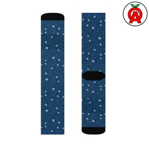 以下が含まれることがあります： 白の飛行機と点線の飛行経路の繰り返し模様が特徴の、ネイビーブルーの靴下。 靴下のかかととつま先は黒です。 旅行をテーマにしたデザインです。