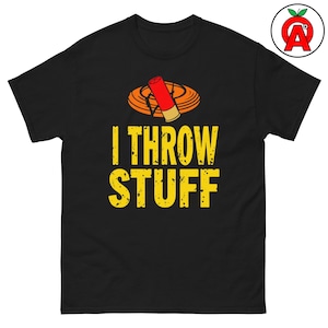 Puede incluir: Camiseta negra con el texto "I THROW STUFF" en fuente amarilla desgastada. Encima del texto hay una ilustración de un plato de arcilla y un cartucho de escopeta. La camiseta es de cuello redondo.