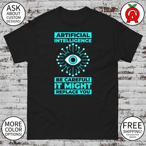 May include: Black t-shirt with the text "ARTIFICIAL INTELLIGENCE" above a graphic of an eye surrounded by a circuit board design. Below the graphic, the text reads "BE CAREFUL! IT MIGHT REPLACE YOU". The shirt also has the text "ASK ABOUT CUSTOM DESIGNS!" and "MORE COLOR OPTIONS!"