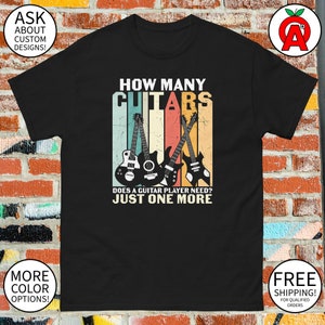 May include: A black t-shirt with a vintage-style graphic of three guitars and the text "HOW MANY GUITARS DOES A GUITAR PLAYER NEED? JUST ONE MORE".