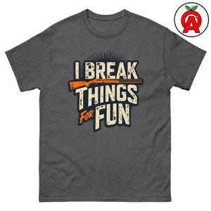 Könnte beinhalten: Ein dunkelgraues T-Shirt mit einem abgenutzten Grafikdesign, auf dem "I Break Things For Fun" steht, und einem stilisierten Bild einer Schrotflinte.