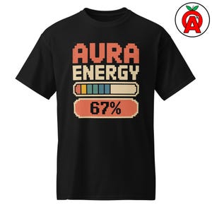 Puede incluir: Camiseta negra con las palabras "AURA ENERGY" en fuente pixelada naranja y beige. Debajo, una barra de progreso y el número "67%" en un estilo similar. La camiseta tiene mangas cortas.