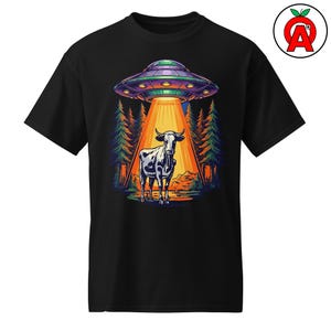 May include: Black t-shirt featuring a colorful graphic of a cow being abducted by a UFO. The design includes a forest backdrop and a bright beam of light shining down on the cow. The UFO is purple and green.
