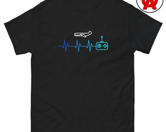 Op de afbeelding: Een zwart t-shirt met korte mouwen en een grafische print van een blauw-naar-turquoise hartslaglijn. Het ontwerp bevat een wit silhouet van een vliegtuig boven de lijn en een lichtblauw icoon van een afstandsbediening aan het einde.
